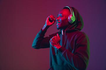 Image showing African-american man\'s portrait with headphones isolated on gradient studio background in neon light