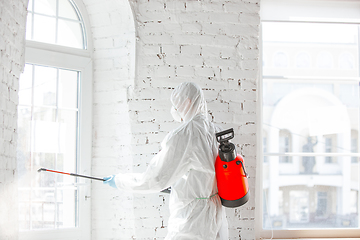 Image showing Coronavirus Pandemic. A disinfector in a protective suit and mask sprays disinfectants in the house or office