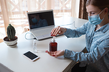 Image showing Young woman in face mask disinfecting gadgets surfaces on her workplace