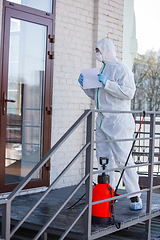 Image showing Coronavirus Pandemic. A disinfector in a protective suit and mask sprays disinfectants in the house or office