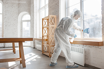 Image showing Coronavirus Pandemic. A disinfector in a protective suit and mask sprays disinfectants in the house or office