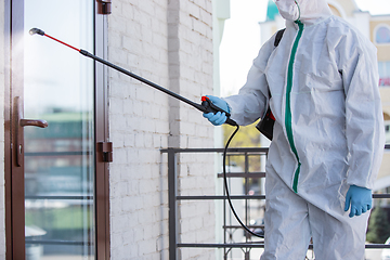 Image showing Coronavirus Pandemic. A disinfector in a protective suit and mask sprays disinfectants in the house or office