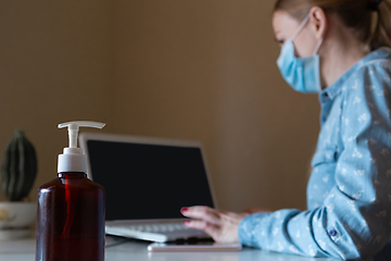 Image showing Young woman in face mask disinfecting gadgets surfaces on her workplace