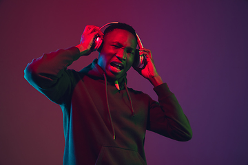 Image showing African-american man\'s portrait with headphones isolated on gradient studio background in neon light