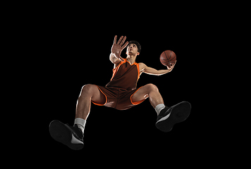 Image showing Young professional basketball player in action, motion isolated on black background, look from the bottom. Concept of sport, movement, energy and dynamic.