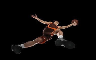 Image showing Young professional basketball player in action, motion isolated on black background, look from the bottom. Concept of sport, movement, energy and dynamic.