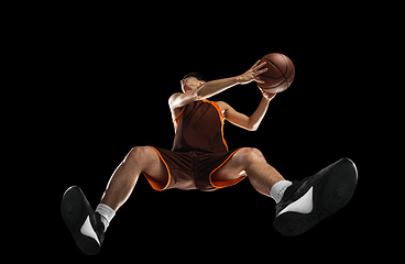 Image showing Young professional basketball player in action, motion isolated on black background, look from the bottom. Concept of sport, movement, energy and dynamic.