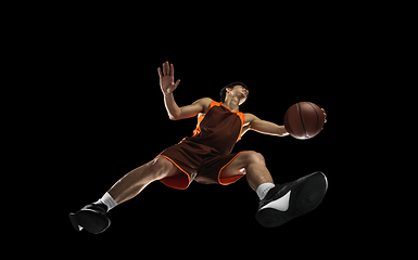 Image showing Young professional basketball player in action, motion isolated on black background, look from the bottom. Concept of sport, movement, energy and dynamic.