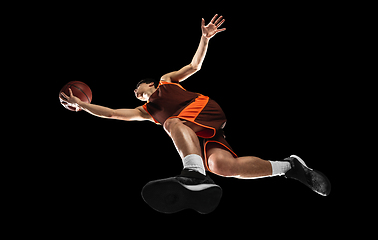 Image showing Young professional basketball player in action, motion isolated on black background, look from the bottom. Concept of sport, movement, energy and dynamic.