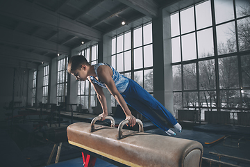 Image showing Little male gymnast training in gym, flexible and active. Caucasian fit little boy, athlete in sportswear practicing in exercises for strength, balance.