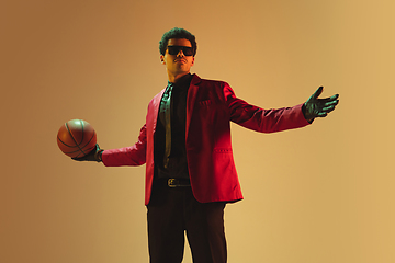 Image showing High-fashion styled man in red jacket playing basketball isolted over brown background