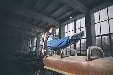 Image showing Little male gymnast training in gym, flexible and active. Caucasian fit little boy, athlete in sportswear practicing in exercises for strength, balance.