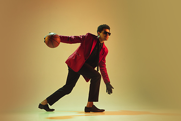 Image showing High-fashion styled man in red jacket playing basketball isolted over brown background