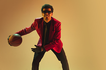 Image showing High-fashion styled man in red jacket playing basketball isolted over brown background