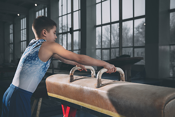 Image showing Little male gymnast training in gym, flexible and active. Caucasian fit little boy, athlete in sportswear practicing in exercises for strength, balance.