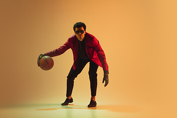 Image showing High-fashion styled man in red jacket playing basketball isolted over brown background