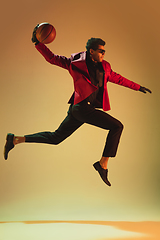 Image showing High-fashion styled man in red jacket playing basketball isolted over brown background