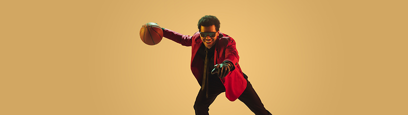 Image showing High-fashion styled man in red jacket playing basketball isolted over brown background