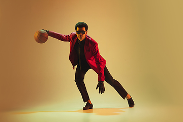 Image showing High-fashion styled man in red jacket playing basketball isolted over brown background