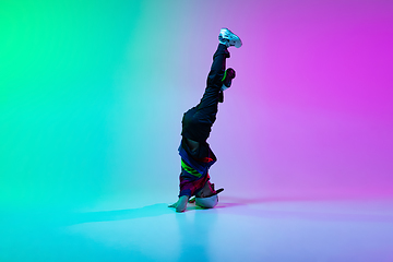 Image showing Beautiful sportive boy dancing hip-hop in stylish clothes on colorful gradient background at dance hall in neon light.