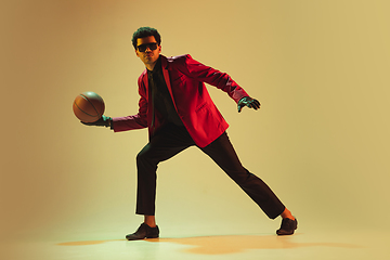 Image showing High-fashion styled man in red jacket playing basketball isolted over brown background