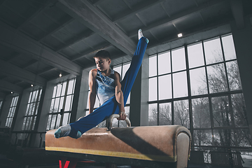 Image showing Little male gymnast training in gym, flexible and active. Caucasian fit little boy, athlete in sportswear practicing in exercises for strength, balance.