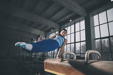 Image showing Little male gymnast training in gym, flexible and active. Caucasian fit little boy, athlete in sportswear practicing in exercises for strength, balance.