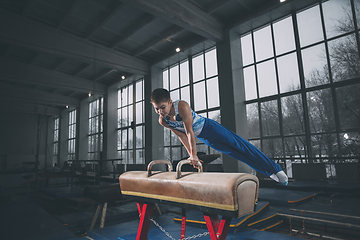 Image showing Little male gymnast training in gym, flexible and active. Caucasian fit little boy, athlete in sportswear practicing in exercises for strength, balance.