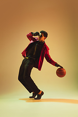 Image showing High-fashion styled man in red jacket playing basketball isolted over brown background