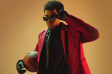 Image showing High-fashion styled man in red jacket playing basketball isolted over brown background