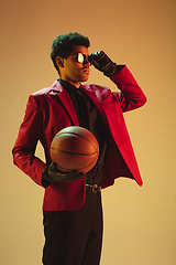 Image showing High-fashion styled man in red jacket playing basketball isolted over brown background