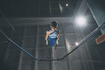 Image showing Little male gymnast training in gym, flexible and active. Caucasian fit little boy, athlete in sportswear practicing in exercises for strength, balance.