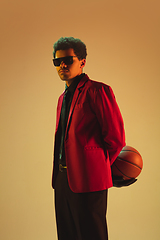 Image showing High-fashion styled man in red jacket playing basketball isolted over brown background