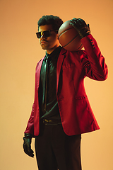 Image showing High-fashion styled man in red jacket playing basketball isolted over brown background