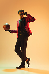 Image showing High-fashion styled man in red jacket playing basketball isolted over brown background