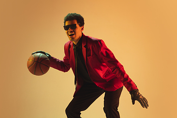 Image showing High-fashion styled man in red jacket playing basketball isolted over brown background