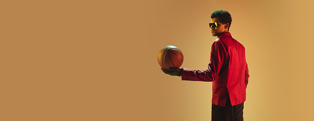 Image showing High-fashion styled man in red jacket playing basketball isolted over brown background