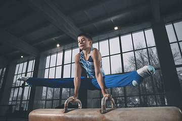 Image showing Little male gymnast training in gym, flexible and active. Caucasian fit little boy, athlete in sportswear practicing in exercises for strength, balance.