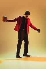 Image showing High-fashion styled man in red jacket playing basketball isolted over brown background