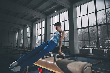 Image showing Little male gymnast training in gym, flexible and active. Caucasian fit little boy, athlete in sportswear practicing in exercises for strength, balance.