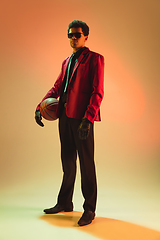 Image showing High-fashion styled man in red jacket playing basketball isolted over brown background