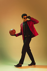 Image showing High-fashion styled man in red jacket playing basketball isolted over brown background