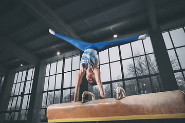 Image showing Little male gymnast training in gym, flexible and active. Caucasian fit little boy, athlete in sportswear practicing in exercises for strength, balance.