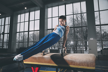 Image showing Little male gymnast training in gym, flexible and active. Caucasian fit little boy, athlete in sportswear practicing in exercises for strength, balance.