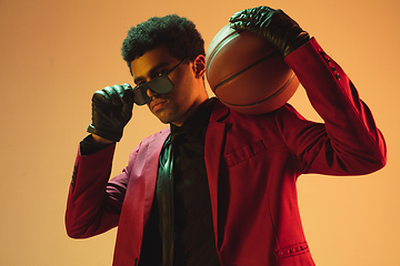 Image showing High-fashion styled man in red jacket playing basketball isolted over brown background