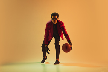 Image showing High-fashion styled man in red jacket playing basketball isolted over brown background