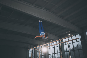 Image showing Little male gymnast training in gym, flexible and active. Caucasian fit little boy, athlete in sportswear practicing in exercises for strength, balance.