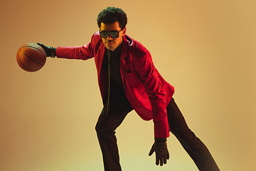 Image showing High-fashion styled man in red jacket playing basketball isolted over brown background