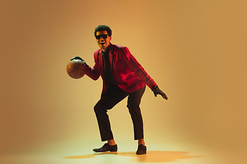 Image showing High-fashion styled man in red jacket playing basketball isolted over brown background