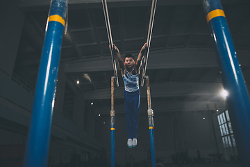 Image showing Little male gymnast training in gym, flexible and active. Caucasian fit little boy, athlete in sportswear practicing in exercises for strength, balance.